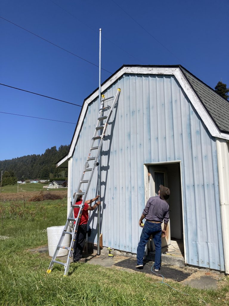 Hired hands installing a 20 foot pole against the side of the barn for mounting a bird laser